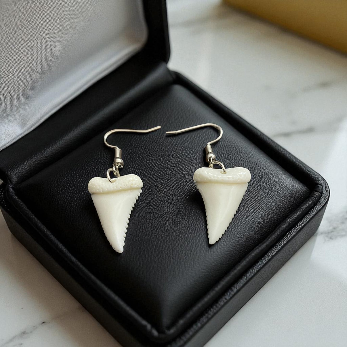 Shark tooth-shaped earrings in a black jewelry box on a marble surface