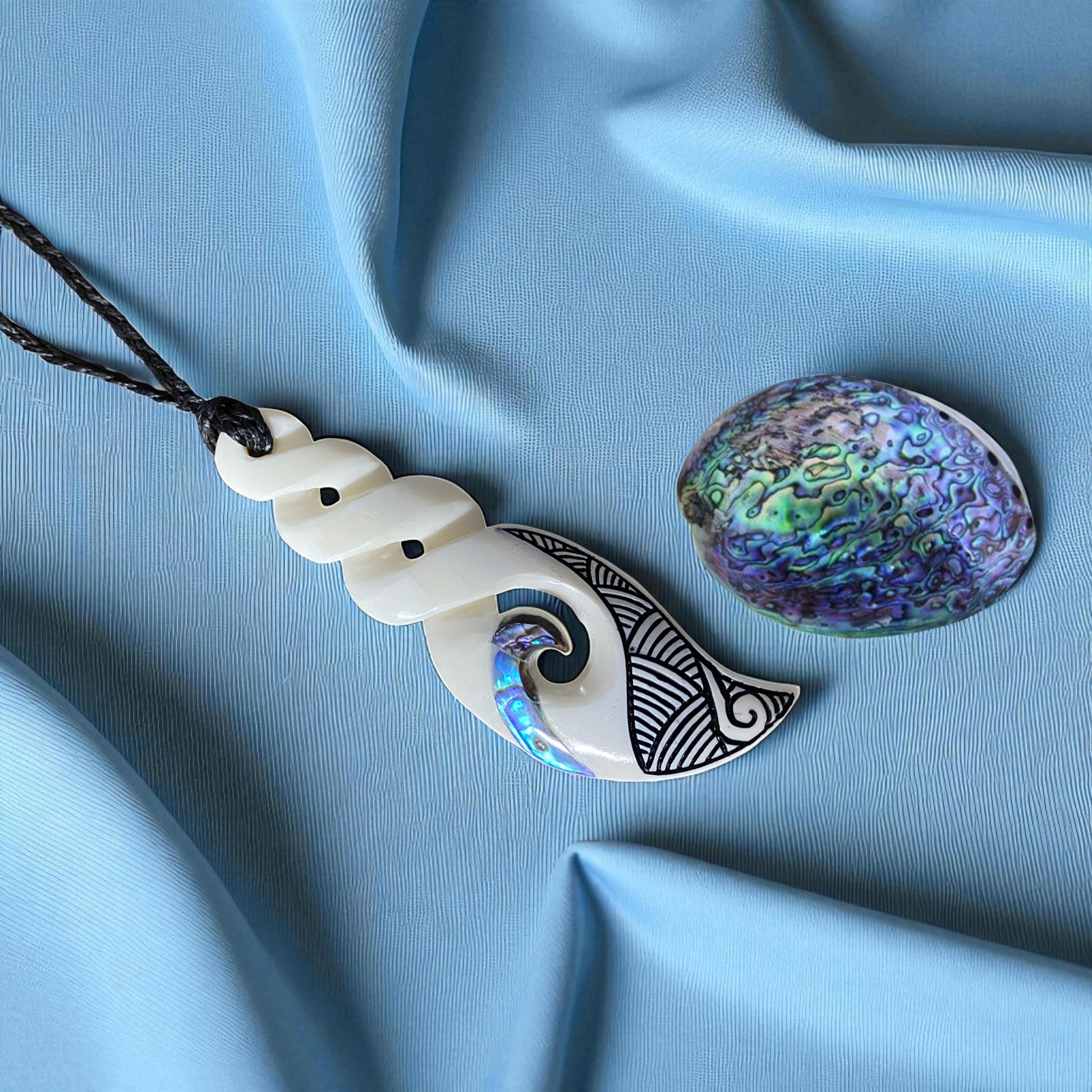 Decorative pendant with wave design and colorful shell on a blue fabric background